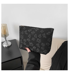 Neceser negro chic con flores en relieve y cremallera dorada sostenido por modelo
