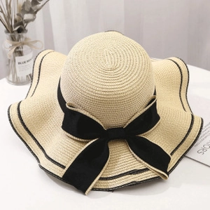 Close-up of beige straw sun hat with black ribbon bow and wavy brim detail