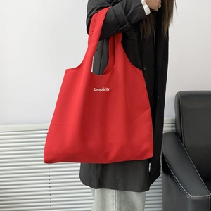 Detailed side view of a large red canvas tote bag with Simplicity lettering on model