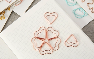 Creative rose gold heart-shaped metal paperclips arranged in flower pattern on paper