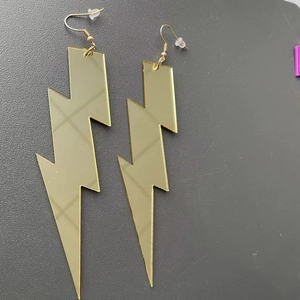Detail of mirror-finish gold lightning bolt earrings with hooks on a grey background