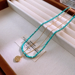 Close-up of blue square stone beads and gold sunburst pendant necklace in a velvet box