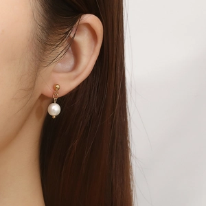 Close-up of minimalist gold C-shaped earrings with pearls and crystals on a model