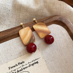 Detail view of square shell and red bead drop earrings on a vintage linen fabric background