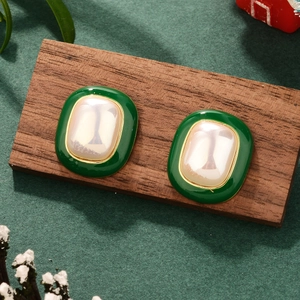 Detailed close-up of vintage style green enamel earrings with square pearls on wood