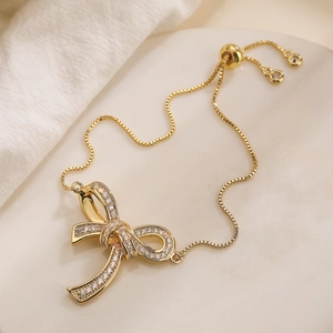 Detail of gold-plated bow bracelet featuring white zircon stones and adjustable slider clasp