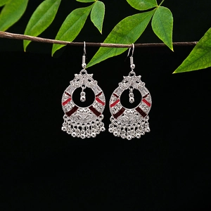 Detail of silver ethnic earrings with red enamel accents and bead tassels on wood