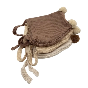 Detailed view of knitted baby hats with pom-poms in coffee, camel, and beige colors