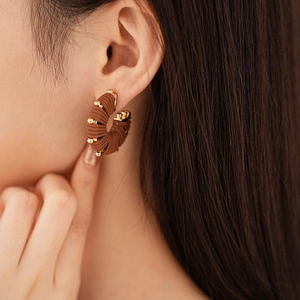 Detail view of brown textured U-shaped earrings with gold beads on a female model
