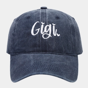 Detailed macro view of the white Gigi embroidery on a washed navy blue cotton baseball cap