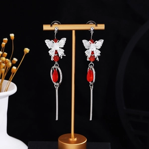 Detail of silver butterfly earrings with red beads and long tassel on a display stand