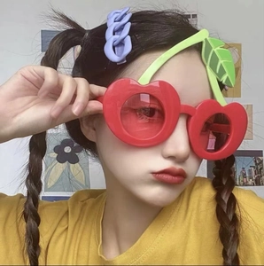 Detail einer roten Kirsch-Sonnenbrille mit grünen Blättern an einem weiblichen Model