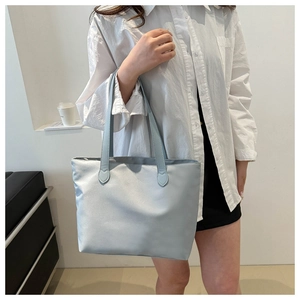 Lifestyle view of a large light blue nylon tote bag worn by a model in a minimal setting