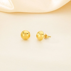 Detailed view of polished golden spherical stud earrings on soft yellow satin background