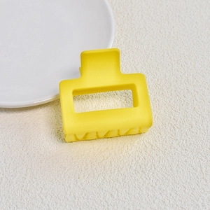 Macro shot of a matte yellow square hair claw clip on a textured white surface