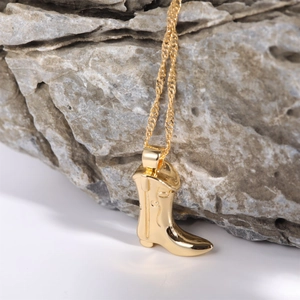 Close-up of gold-plated cowboy boot pendant necklace on a natural stone background