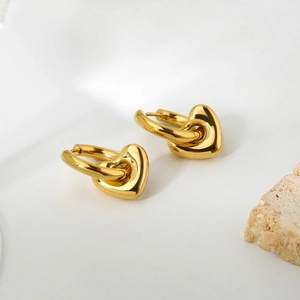 Detail of heart pendant earrings in 14k gold-plated finish on minimalist white background