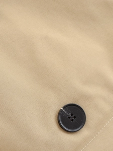 Detailed close-up of khaki twill fabric texture and black buttons on a short trench coat