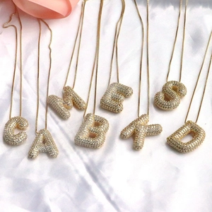Chubby gold-plated copper letter necklaces with iced-out zircon pave on white silk background