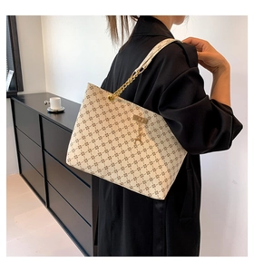 Detail of monogram tote bag featuring gold chain strap and deer pendant on cream leather