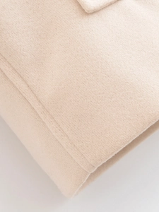 Detailed close-up showing the precise stitching and wool texture of the beige short coat