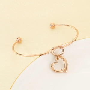 Detail of rose gold knot bangle with a hollow heart pendant on a white jewelry tray