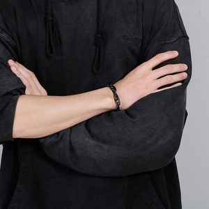 Gros plan du bracelet gourmette pour homme en acier noir porté sur le poignet sur un sweat