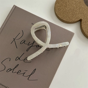 Dettaglio di un fermaglio per capelli in acetato bianco perlato su sfondo minimal