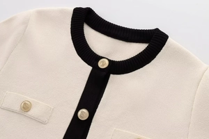 Detail of cream knit cardigan with black contrast trim and gold embossed metal buttons