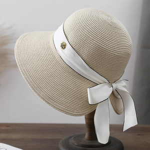 Detailed macro view of beige straw hat with white silk ribbon bow and golden rose badge