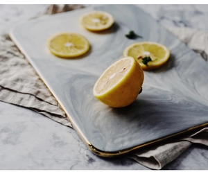 Top view of marble pattern ceramic tray with gold rim on grey linen and fresh lemons