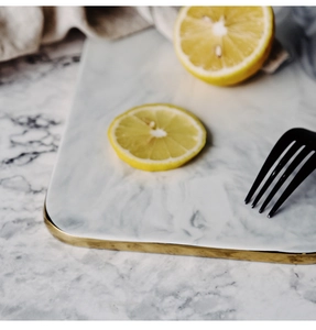 Top view of rectangular marble ceramic tray with gold rim, lemon slices and black fork