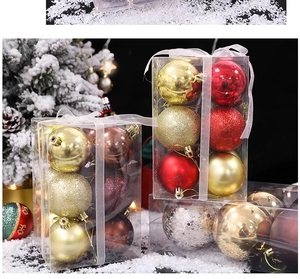 Detail of red and gold Christmas ball ornaments in a clear gift box by a snowy tree