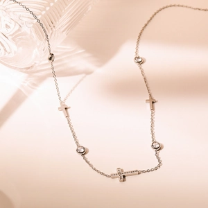 Elegant silver titanium necklace with zircon cross pendant draped on a glass bottle