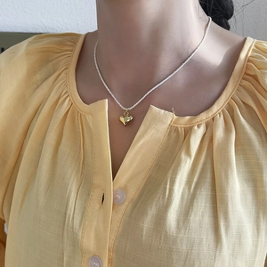 Detail shot of a golden heart pendant necklace on a soft yellow linen fabric background