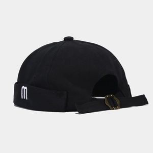 Close-up of black cotton brimless cap with white m embroidery and bronze metal adjustment buckle
