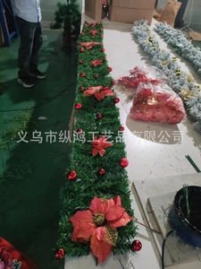 Close-up of green Christmas garland with festive red silk flowers and shiny red ornaments