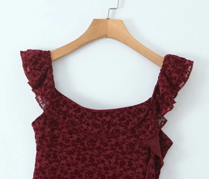 Close-up of wine red velvet top featuring ruffled neckline and intricate lace cutouts