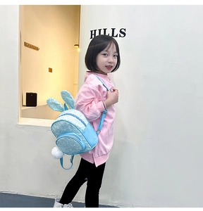Toddler girl wearing light blue sequin backpack with cute bunny ears in a bright room