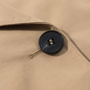 Detailed macro view of black buttons and khaki twill fabric on women's cropped trench coat
