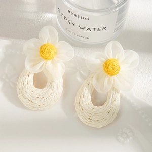 Close-up of handmade raffia woven earrings with elegant white mesh flowers and yellow stamens