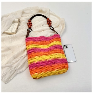 Detail of rainbow straw bucket bag featuring dark leather straps and decorative wooden beads