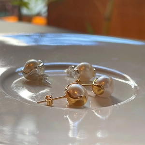 Detailed view of gold and silver pearl stud earrings on a white ceramic plate