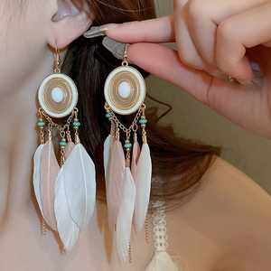 Detail of bohemian gold feather tassel earrings with white beads and pink plumage accents