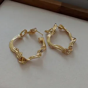 Modern twisted geometric gold hoop earrings with textured finish shown on a vintage background