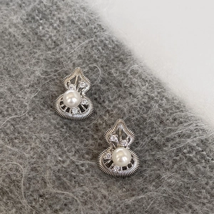 Macro shot of silver gourd stud earrings with central pearl and sparkling zircon accents
