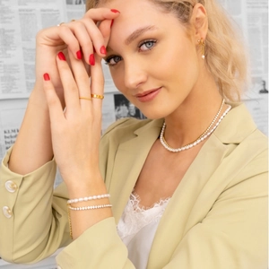 Detail of layered gold necklaces and pearl bracelets worn by a model against newspaper print