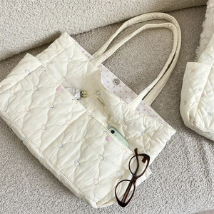 Detail of cream quilted tote bag showing colorful heart stitching and spacious interior