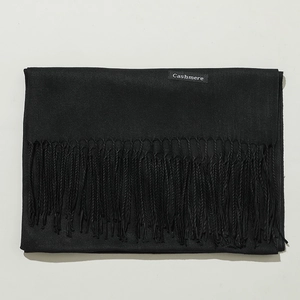 Detail view of the folded black cashmere scarf with fringe edges and quality fabric label