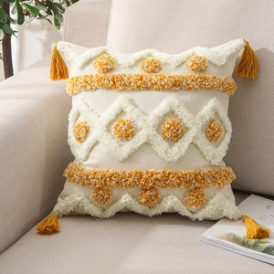 Close-up of tufted bohemian cushion cover with yellow tassels on a beige sofa
